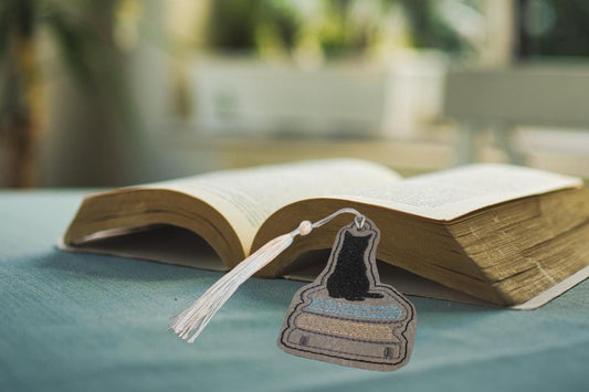 Open book with a bookmark featuring a cat on books, placed on a blue surface with a blurred natural background.