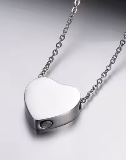 Heart-shaped silver urn pendant on a chain against a gray background