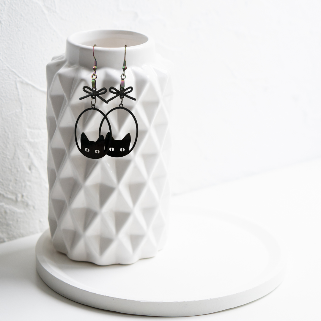White geometric vase with black cat-shaped earrings on a white background