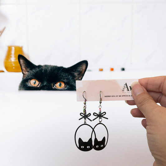 Cat looking at cat-shaped earrings held by a hand