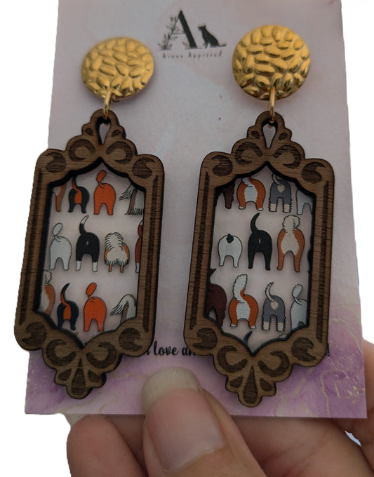 Earrings with dog butts themed design held against a card background