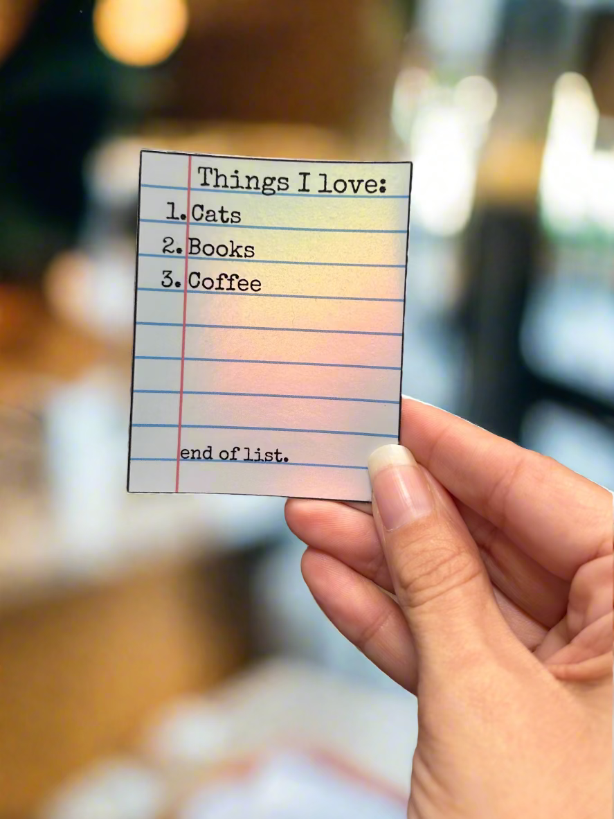 Hand holding a sticker with 'Things I love' list in a coffee shop