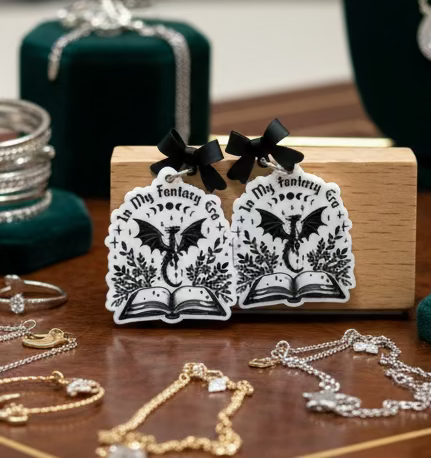 Black and white dragon book earrings on a wooden stand with 'In My Fantasy' text.