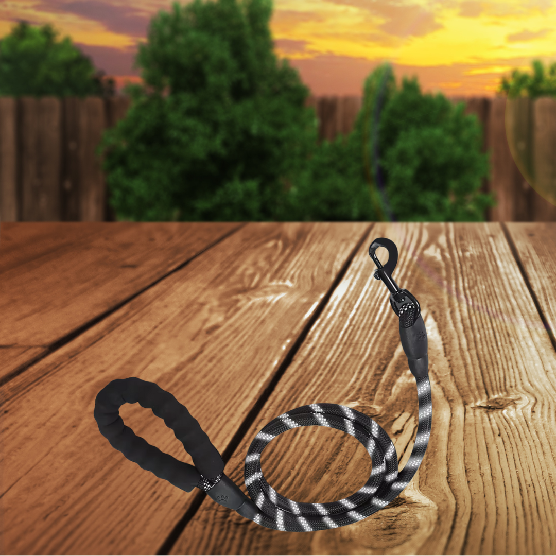Dog leash with black and gray pattern on a wooden surface with a sunset background