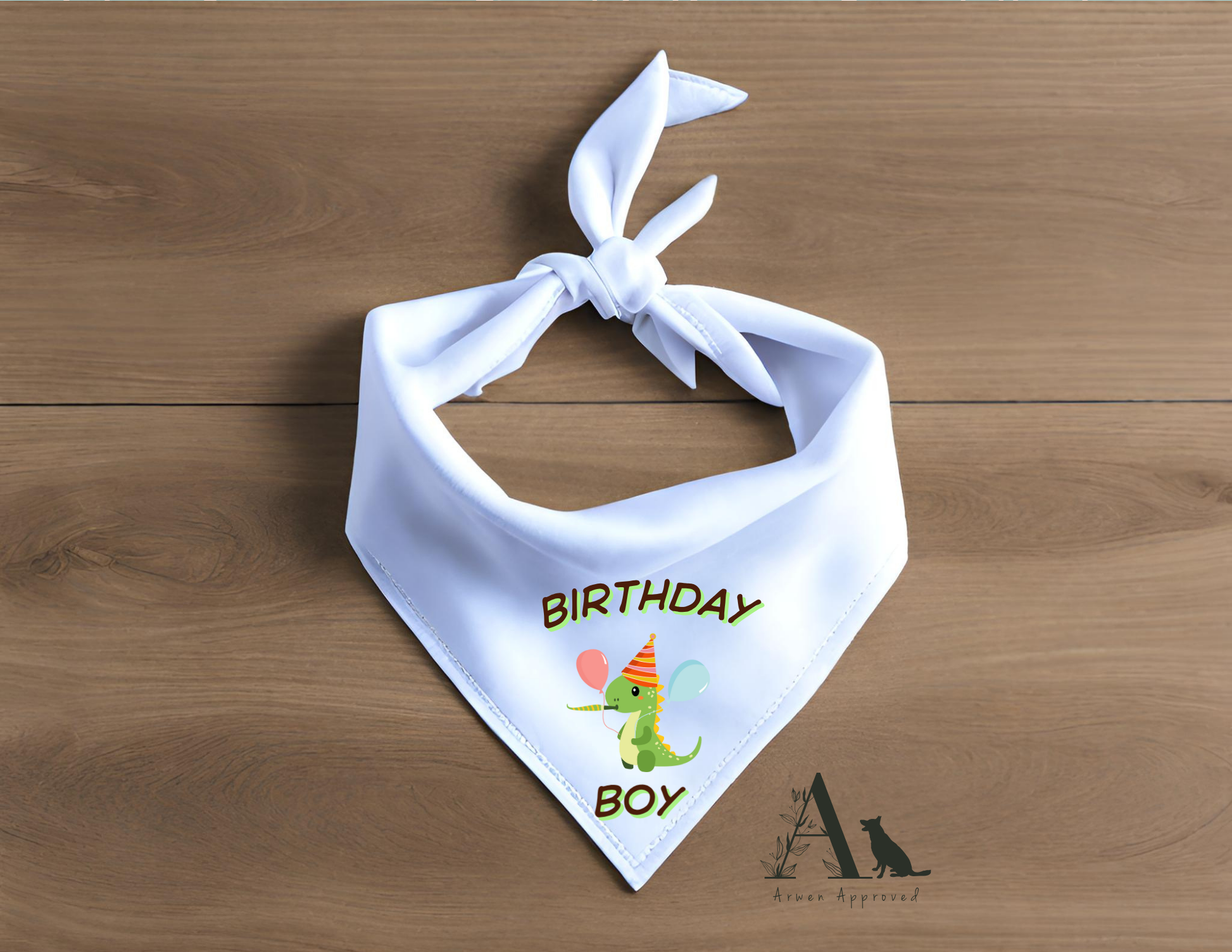 White bandana with 'Birthday Boy' text and dinosaur graphic on a wooden surface