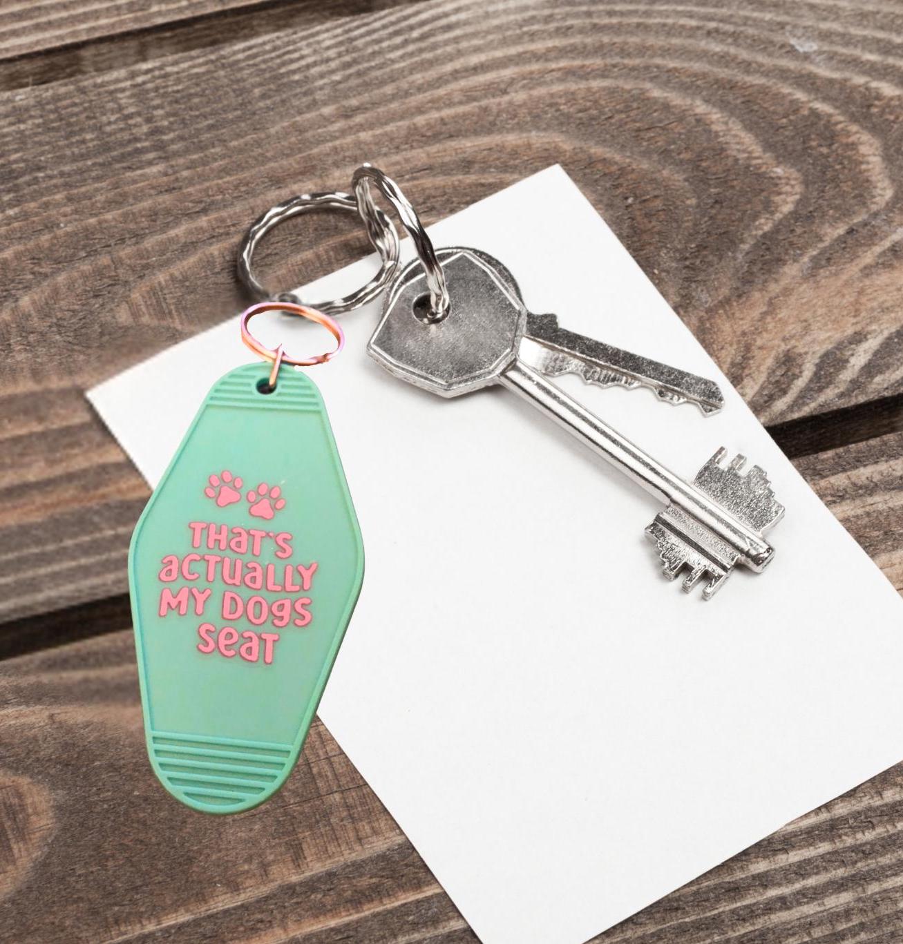 Keychain with paw prints and "that's actually my dogs seat" text on a wooden surface