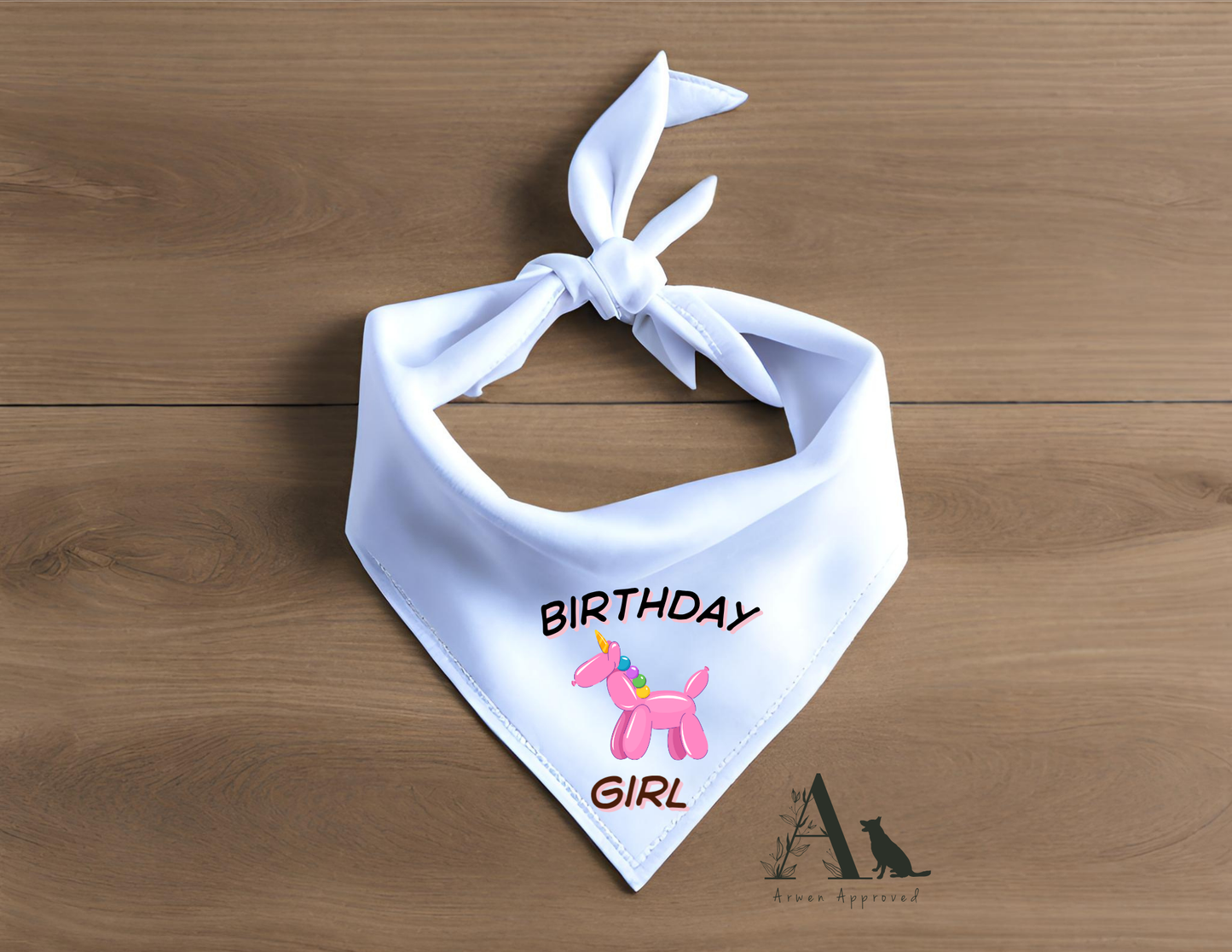 White dog bandana with 'Birthday Girl' text and pink dog graphic on a wooden surface