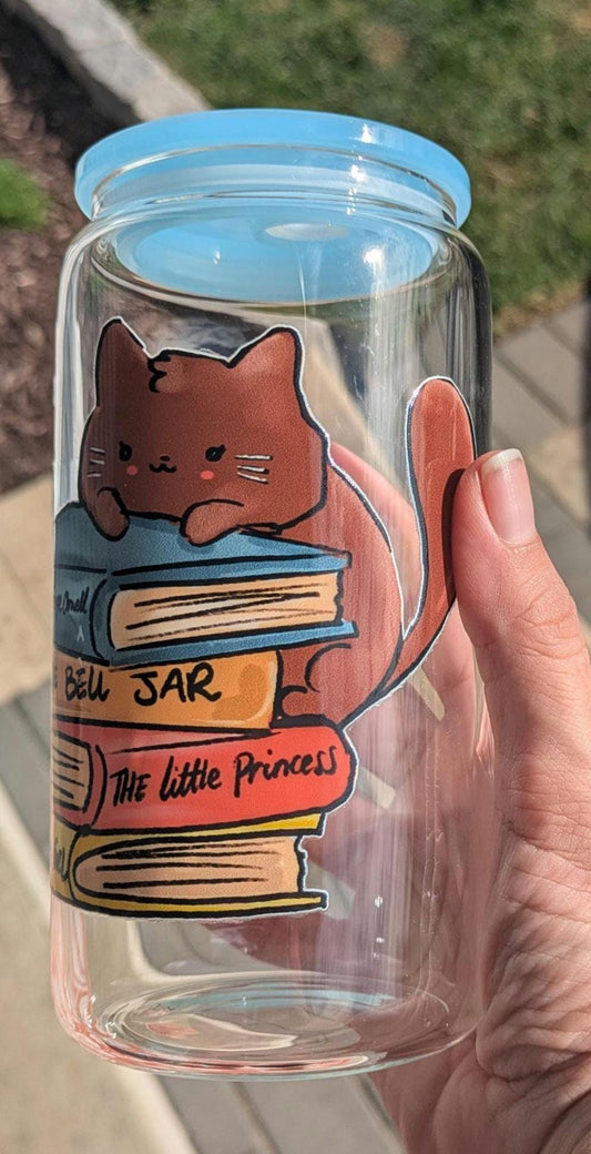 Glass jar with a cat design and text, held by a hand outdoors.