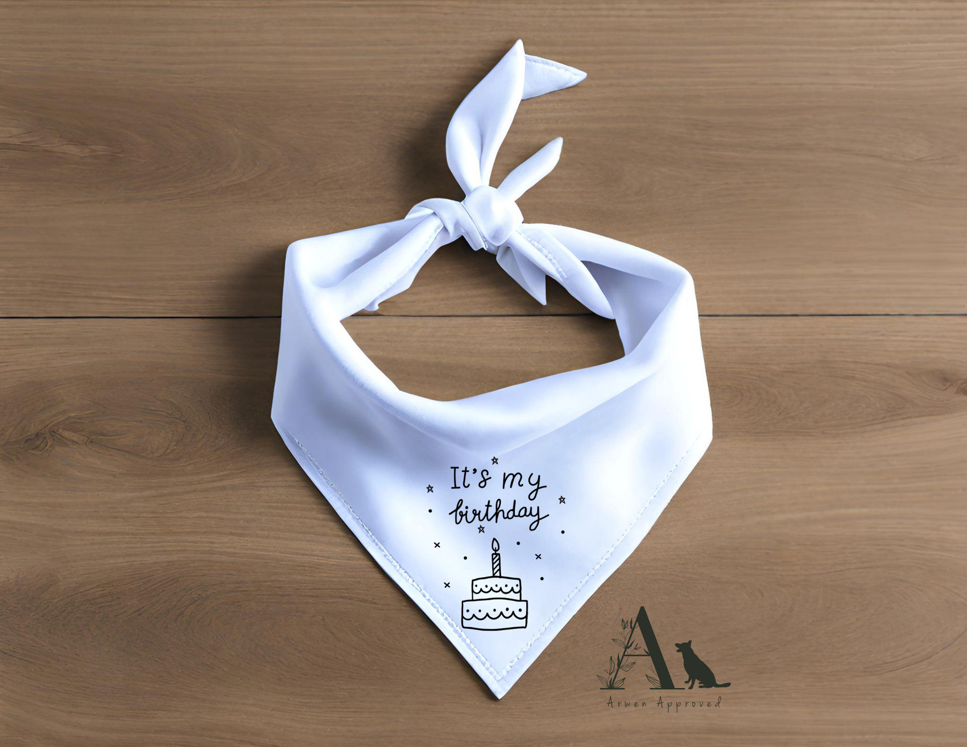 White dog bandana with 'It's my birthday' and cake illustration on a wooden surface