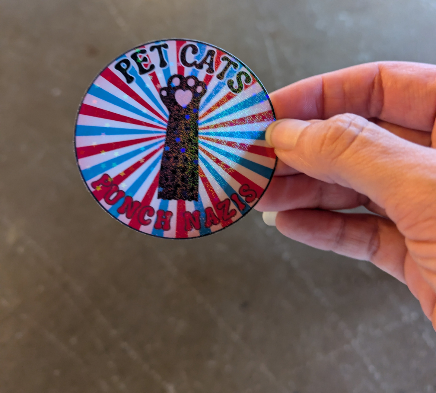 Person holding a sticker with a cat paw and the text pet cats punch nazis