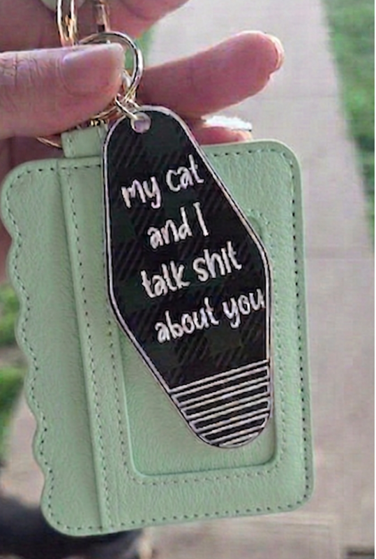 Mint green keychain with black tag saying 'My cat and I talk shit about you' held by a hand.