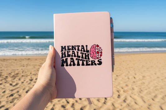 A person holding a notebook with 'Mental Health Matters' illustration on it on a beach