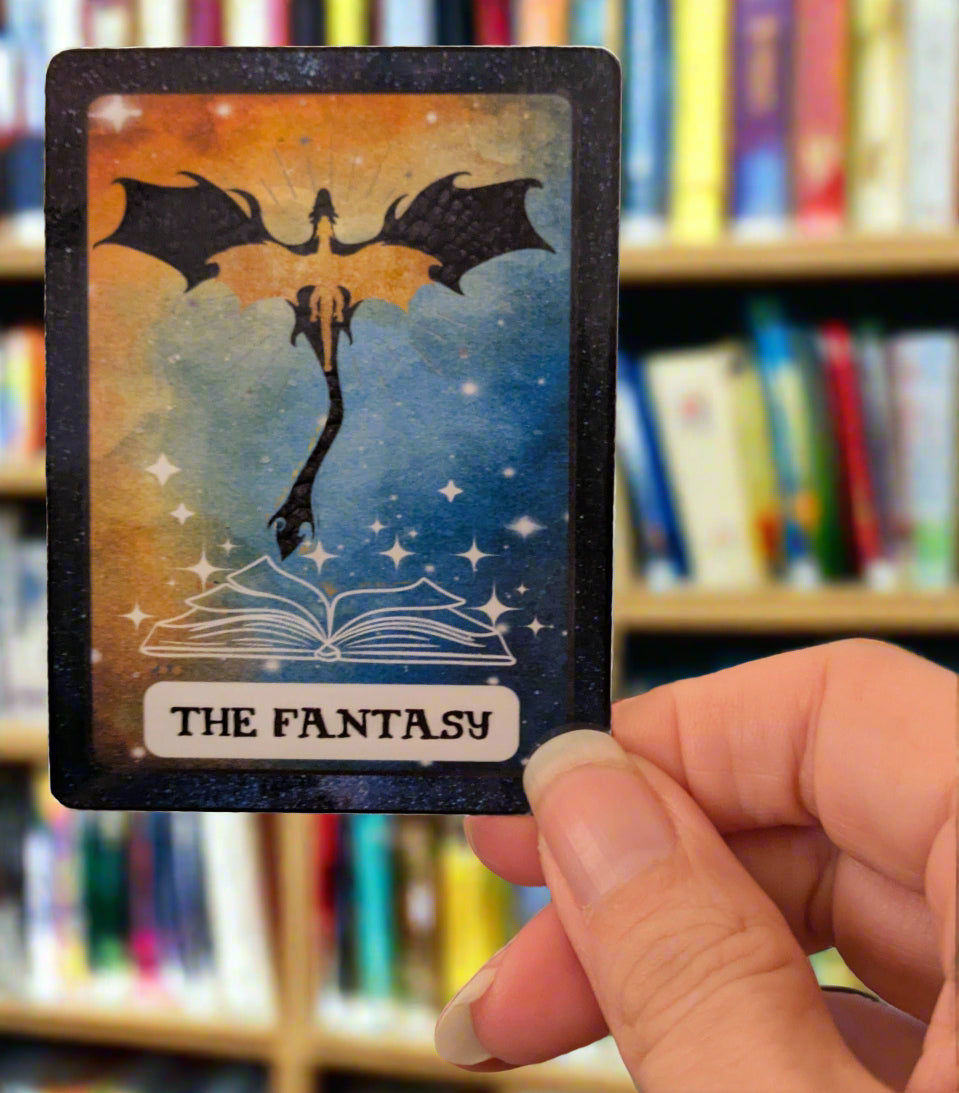 Sticker with a dragon and book design held by a hand in an indoor setting.