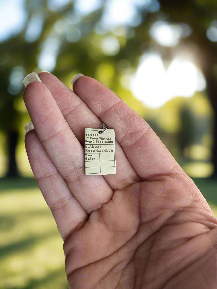 Hand holding a small rectangular necklace with text on a blurred background