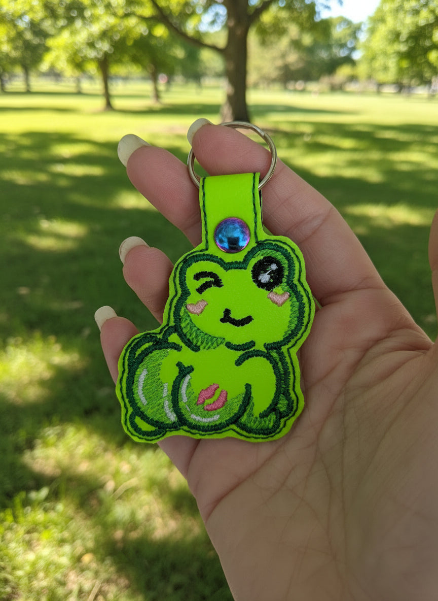 Hand holding a green cartoon frog keychain with a blurred background