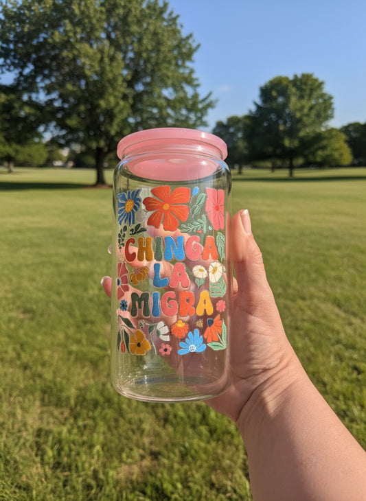 Clear tumbler with colorful floral designs and text held by a hand outdoors.