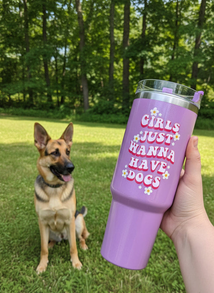 Purple tumbler with text 'Girls Just Wanna Have Dogs' held by a person indoors.