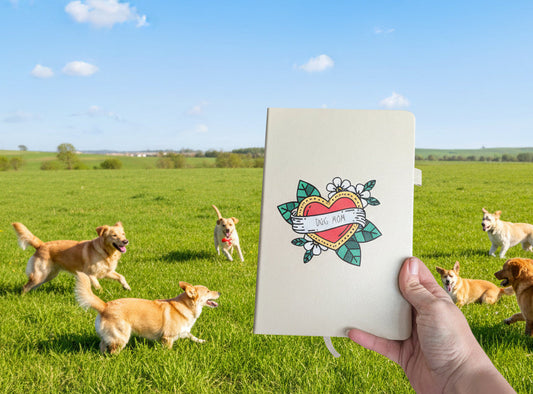 Person holding a journal with a dog mom decal on it in a field with dogs