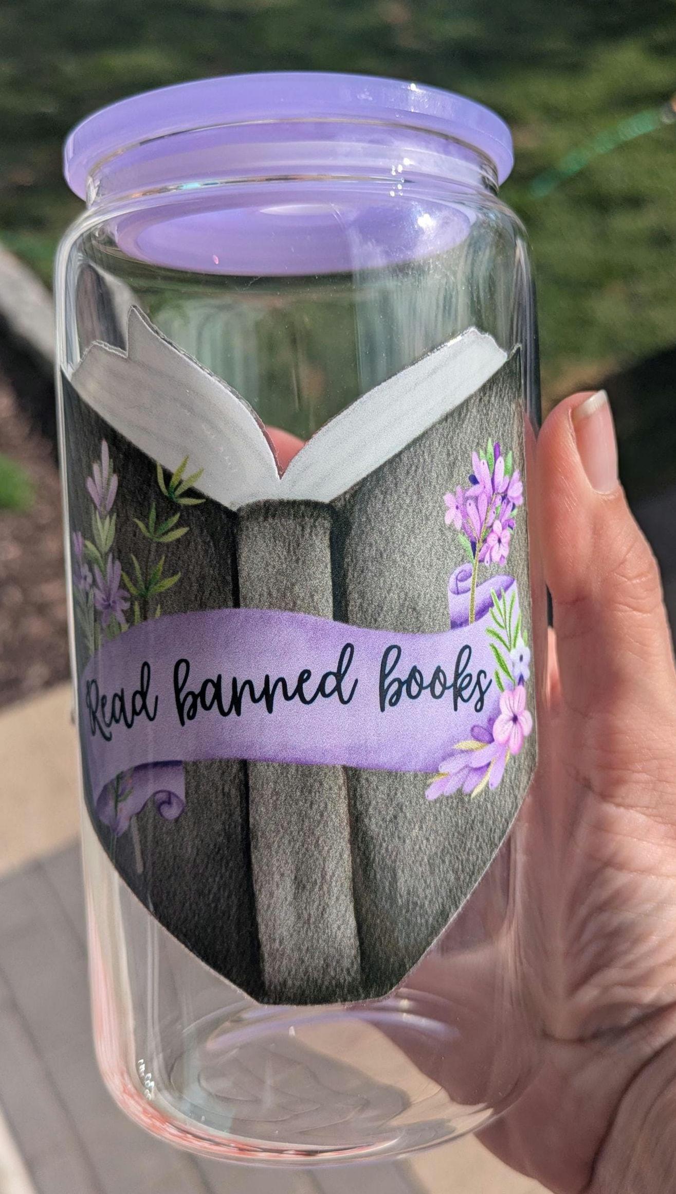 Glass cup with a purple lid and book-themed design, held by a hand.