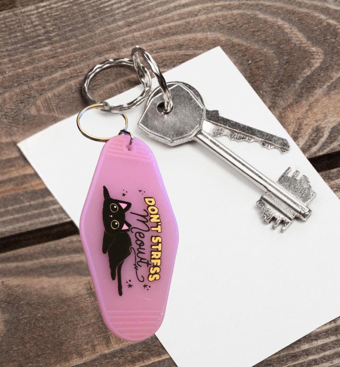 Pink keychain with black cat design and "don't stress meowt" text, attached to keys on a wooden surface.