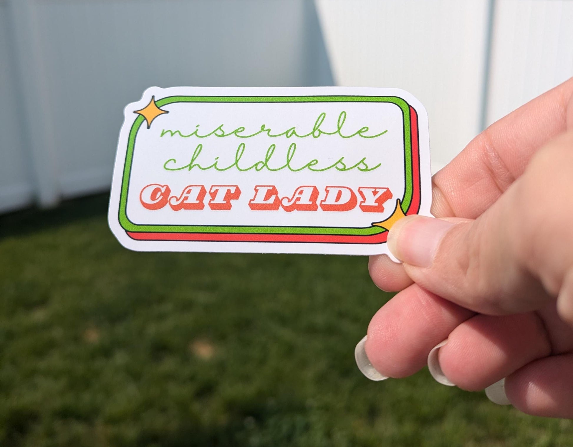 Person holding a rectangular sticker that says miserable childless cat lady