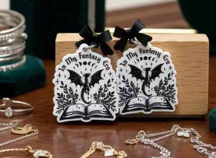 Black and white dragon book earrings on a wooden stand with 'In My Fantasy' text.