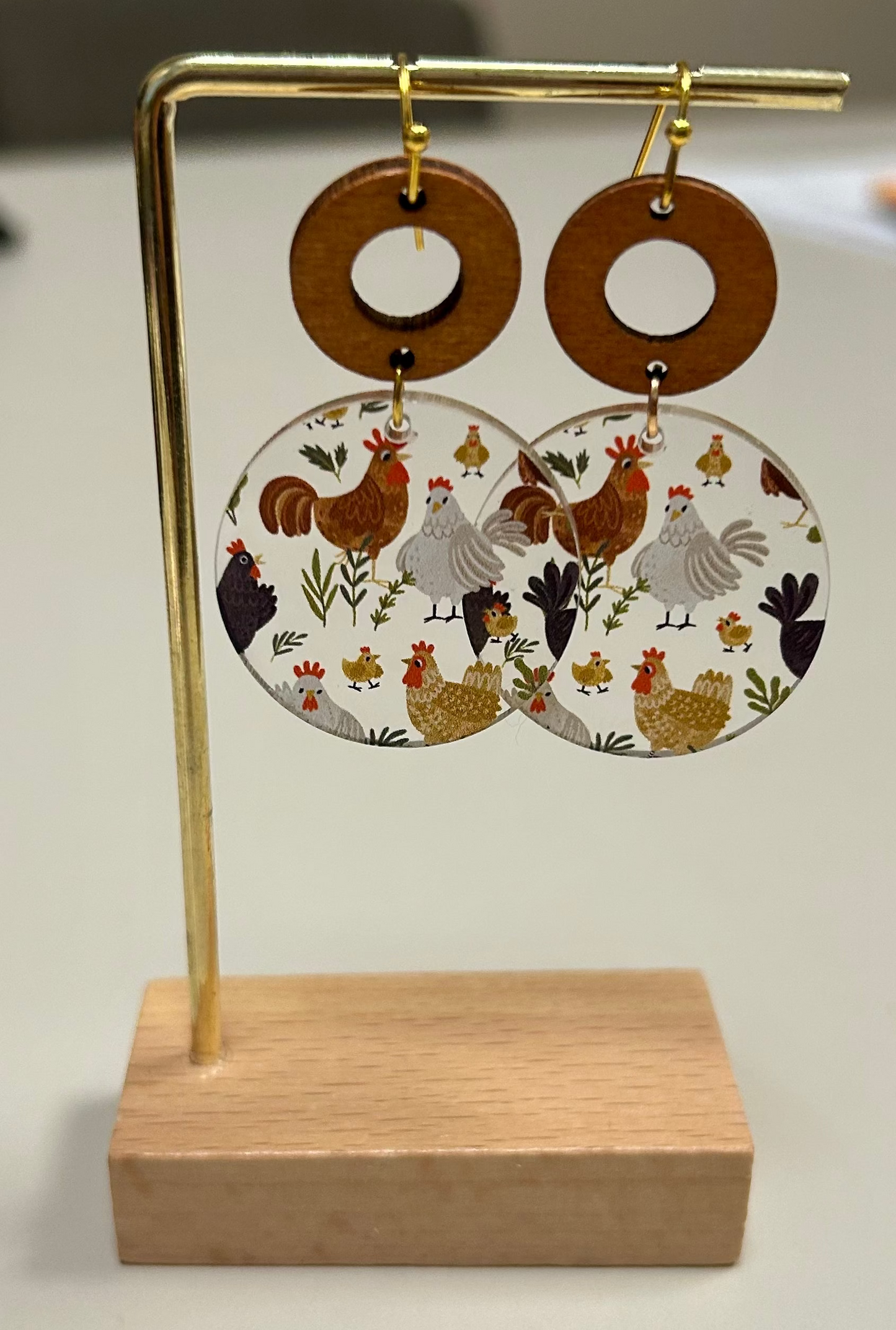 Pair of earrings with chicken design on a wooden stand against a neutral background