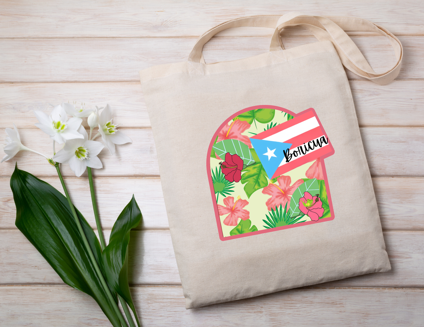 Tote bag with floral design and 'Boricua' text and Puerto Rican flag on a wooden surface with flowers.