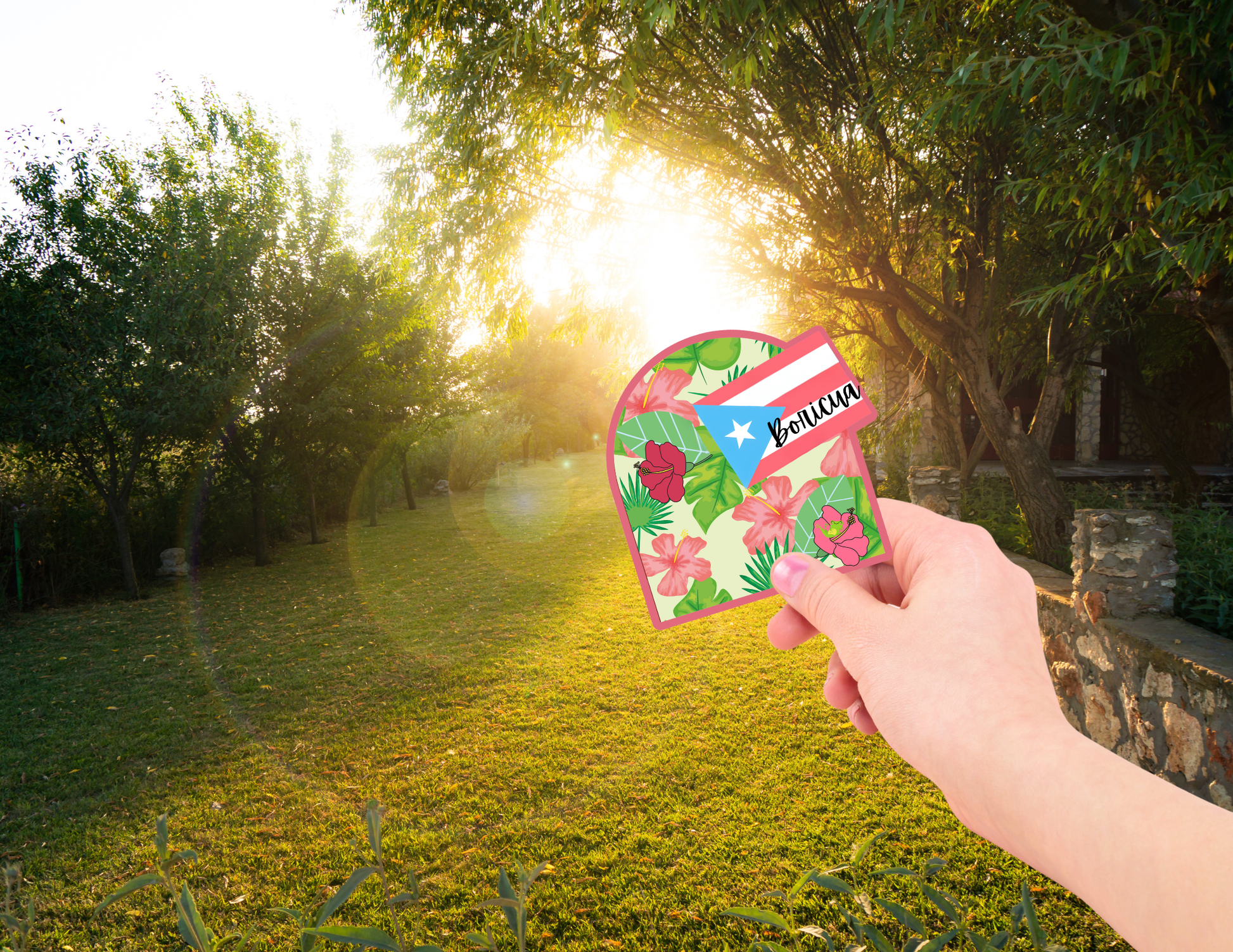 Hand holding a Puerto Rico sticker with a floral design and a flag, set against a natural background with trees and sunlight.