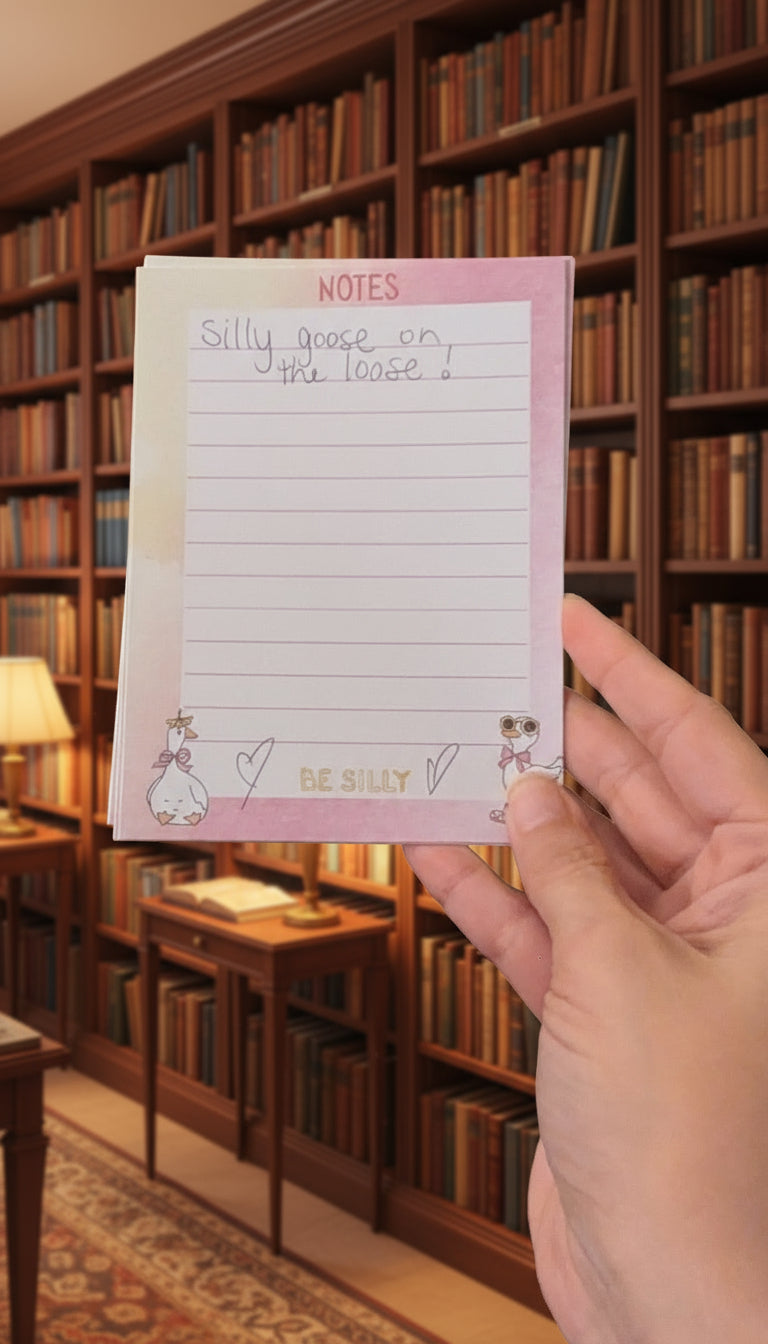 Hand holding a pink notepad inside of a library