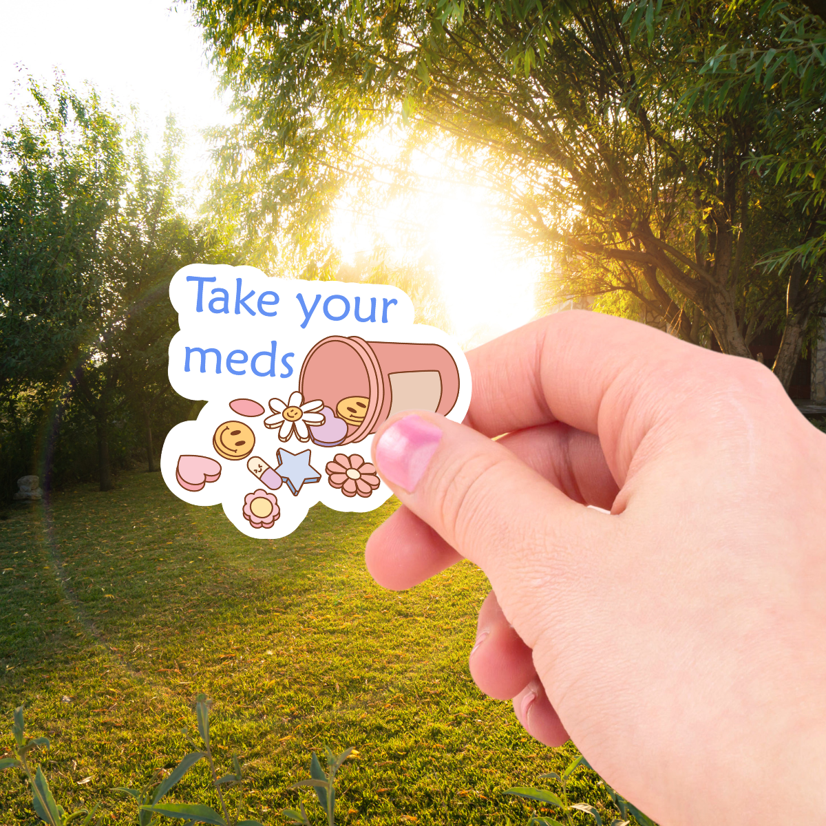 Hand holding a sticker with 'Take your meds' text against a nature background