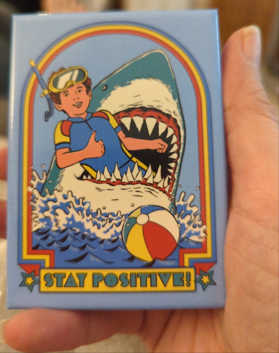 Magnet with a design of a person in a swimsuit surrounded by a shark, with 'Stay Positive!' text.