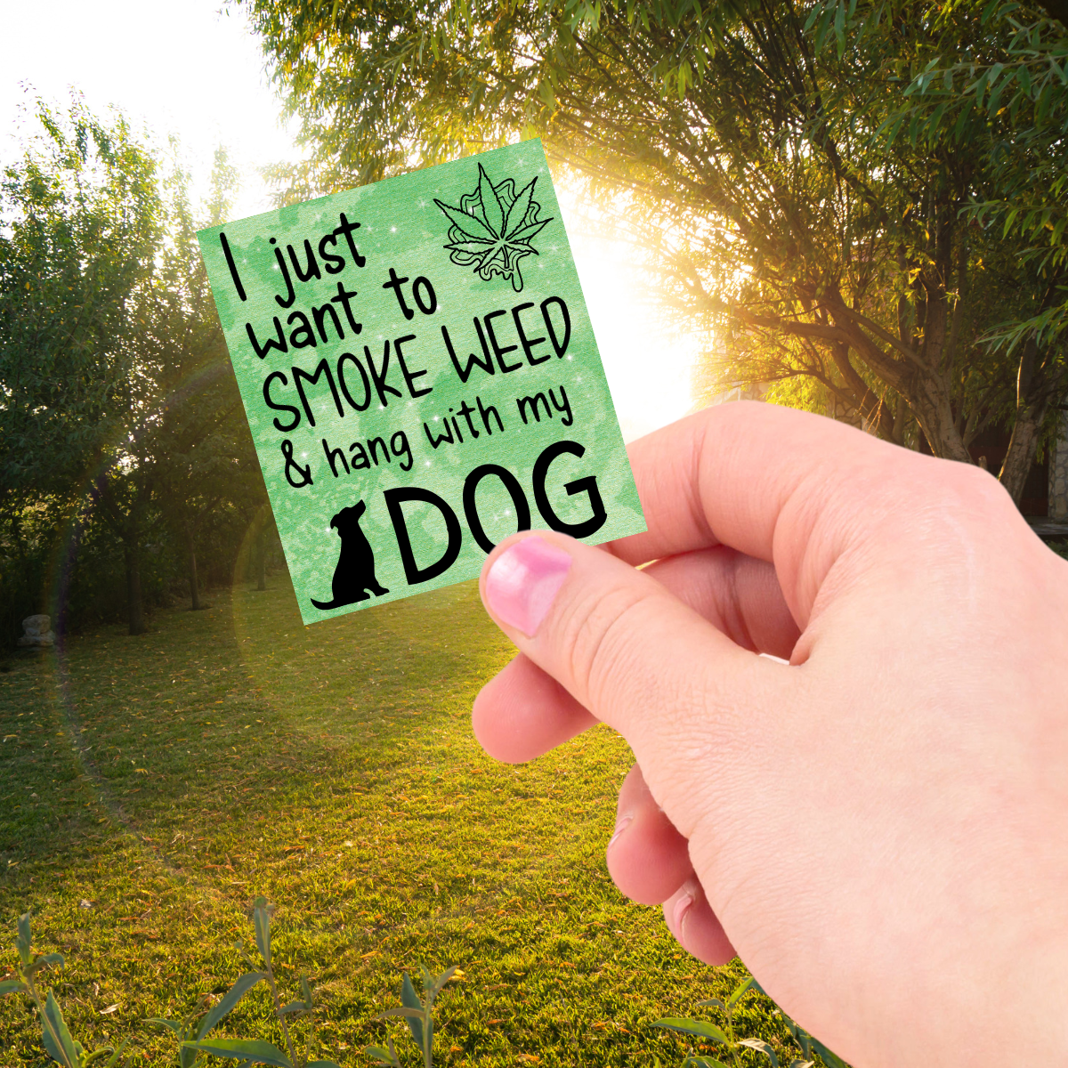 Hand holding a green sticker with text in a park setting
