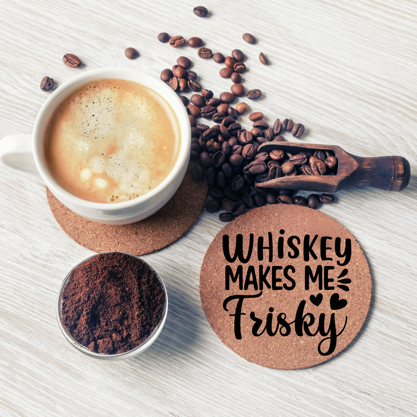 Round cork coaster with text "Whiskey makes me frisky" on a table with a coffee cup, and coffee beans.
