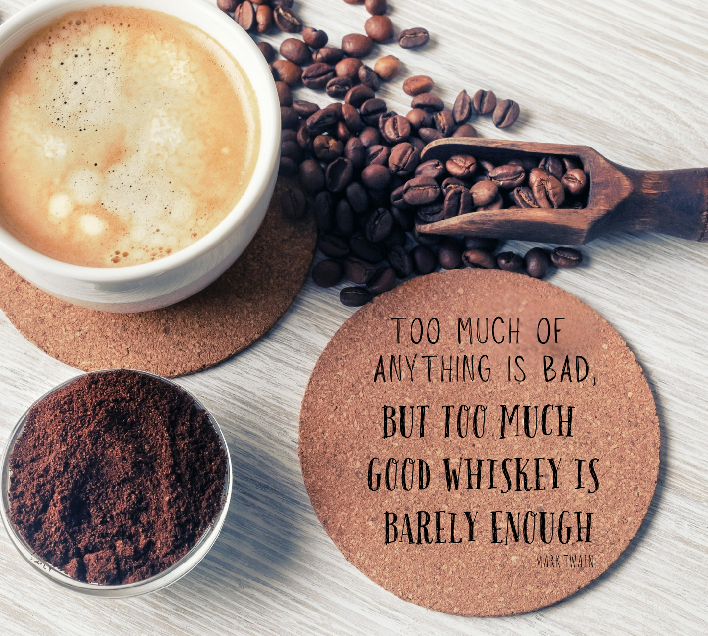 Round cork coaster with text "Too much of anything is bad, but too much good whiskey is barely enough" on a table with a coffee cup, and coffee beans.